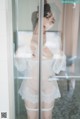 A woman in a white lingerie standing in front of a glass door.